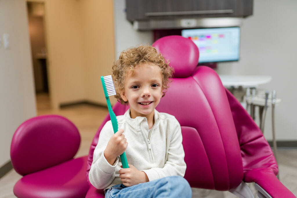 Young boy sitting in dental chair holding a giant green toothbrush