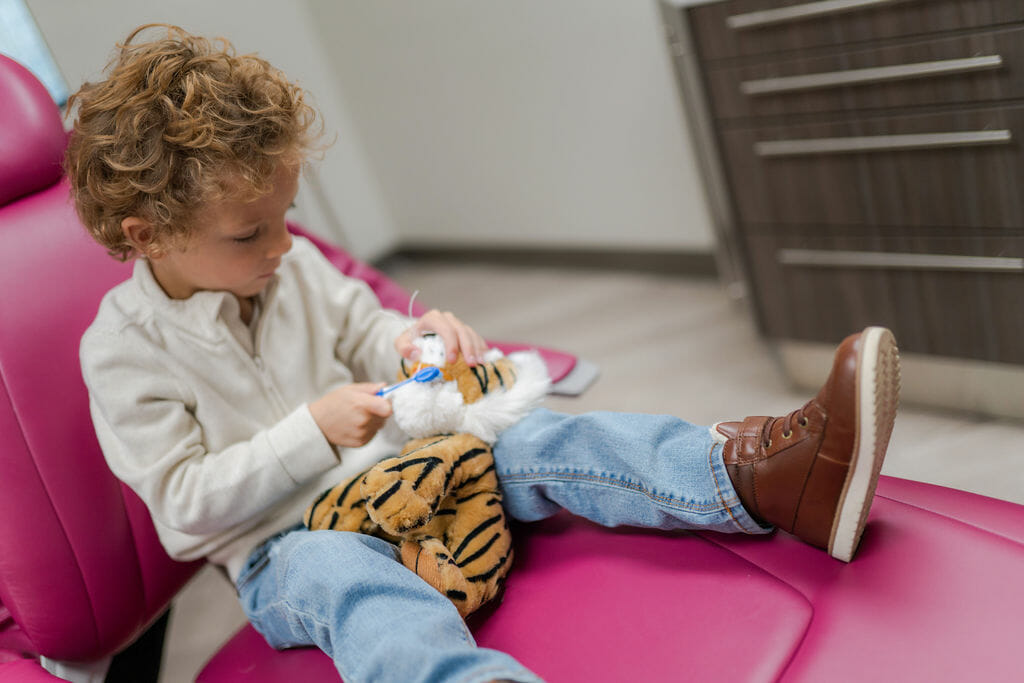 Boy sitting in dental chair brushing stuffed animal's teeth