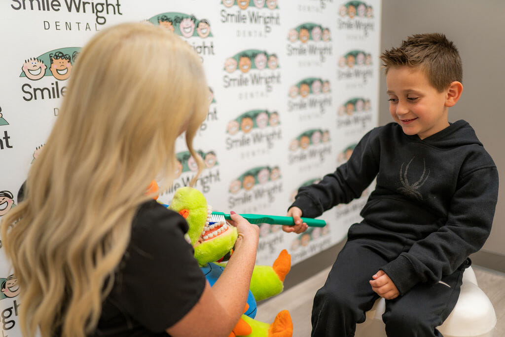 Boy brushing plush dinosaur's teeth with a giant toothbrush