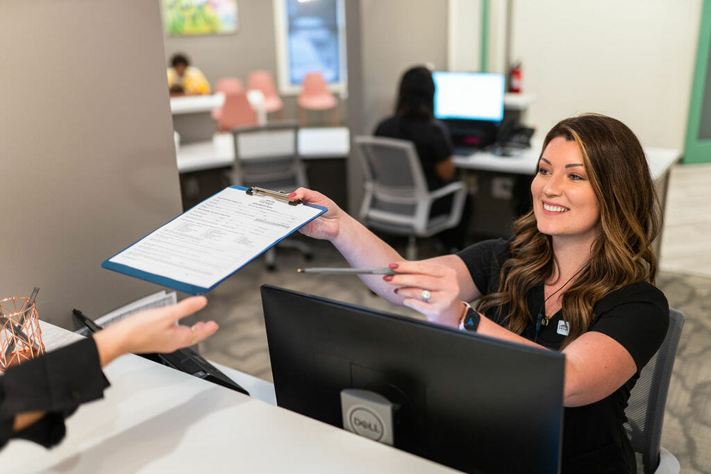 Front desk team member handing clipboard with paperwork to patient